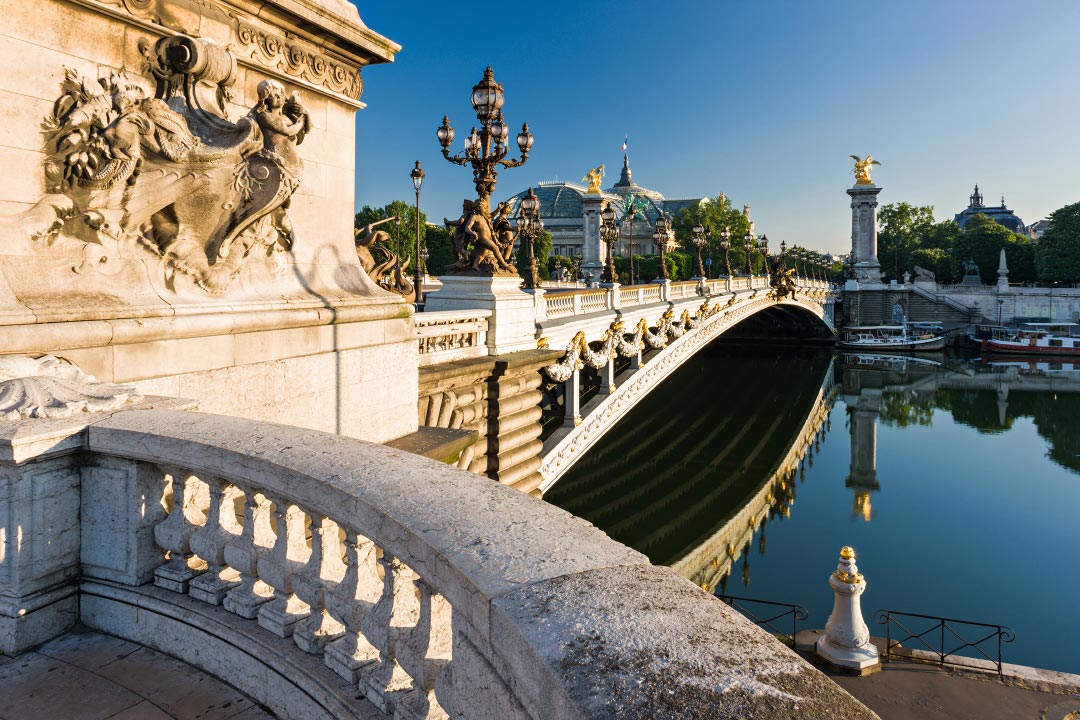 Le pont Alexandre III se reflète dans la Seine, calme, avant la première péniche.